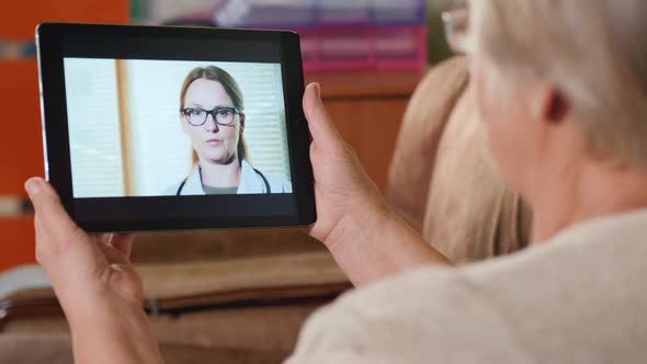 Senior Adult Woman Consults Family Doctor Via Video Link, Holds Tablet alt