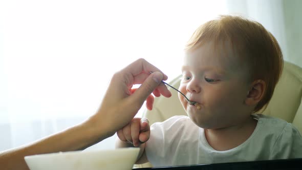 Baby Eating Puree with Spoon. Close Up of Infant Baby Face Eat Baby Food. Mother Feeding Child