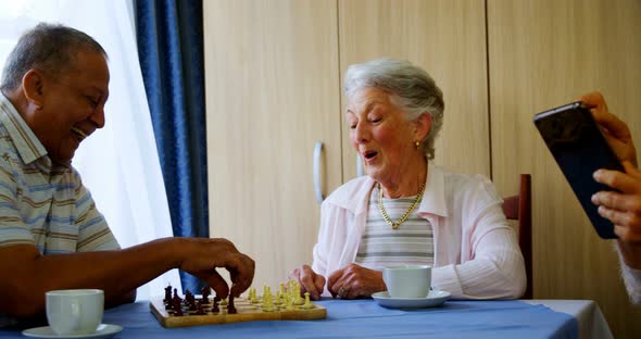 Senior woman using digital tablet while her friends playing chess 4k alt