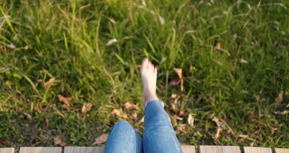 Woman sitting on the wooden walking path and swing the legs alt