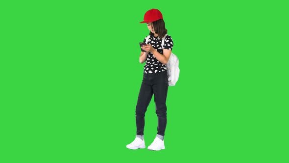 Young Girl Wearing a Backpack and Using Smartphone on a Green Screen Chroma Key alt