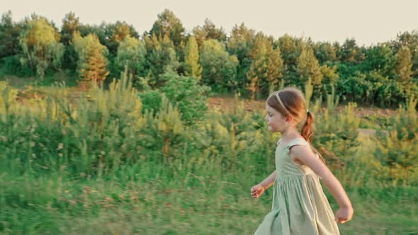 Cute Little Girl in a Green Summer Dress with a Smile Runs Across the Lawn to Meet Dad the Father