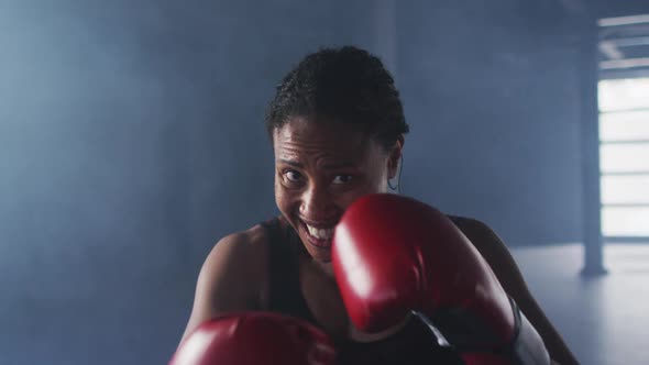 African american woman wearing boxing gloves training throwing punches in empty room alt