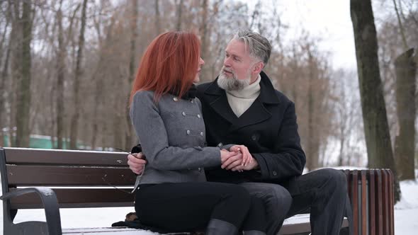 an adult gray-haired man sits on a bench in the park with his girlfriend alt
