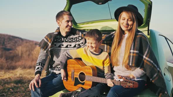 Family Plays Guitar and Sings Songs While Sitting on the Hatchback of the Car alt