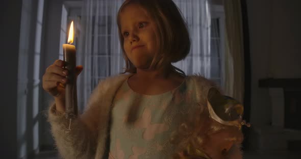 Close-up Portrait of Strange Caucasian Girl Blowing Out Candle and Holding Doll in Other Hand alt