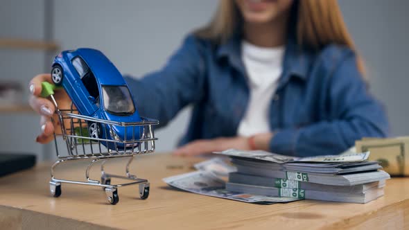 Woman Hands Rolling Shopping Cart with Car on the Table. alt