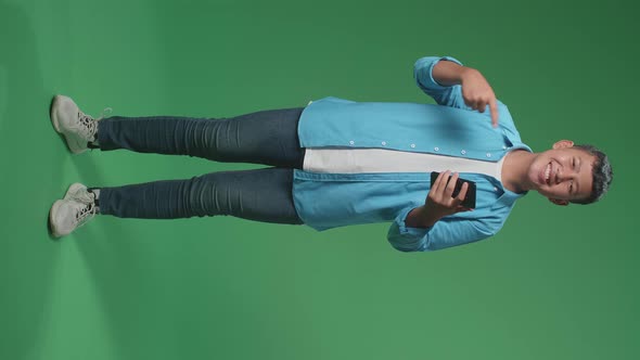 Full Body Of Asian Boy Use Mobile Phone And Pointing To Smart Phone In The Green Screen Studio alt