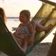 Young Mother Sitting with Her Daughter in a Hammock on the Beach Laughing and Smiling Against the - VideoHive Item for Sale
