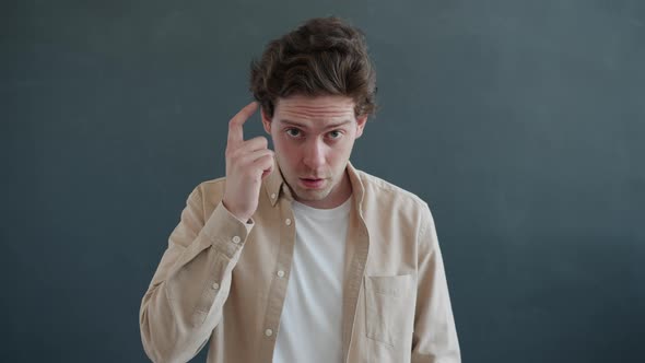 Slow Motion Portrait of Serious Guy Touching Head with Forefinger Asking Are you Crazy alt