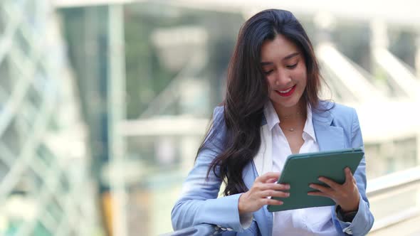 4K Asian businesswoman working on digital tablet while walking city street
