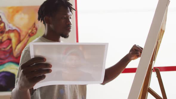 African american male painter painting from photograph on canvas in artist studio alt
