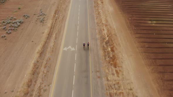 top shot drone aerial tracking shot of two professional road cycelists starting their ride riding at alt