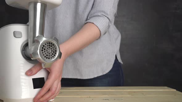 The girl puts an electric meat grinder on the table and shows a nozzle for cooking sausages alt