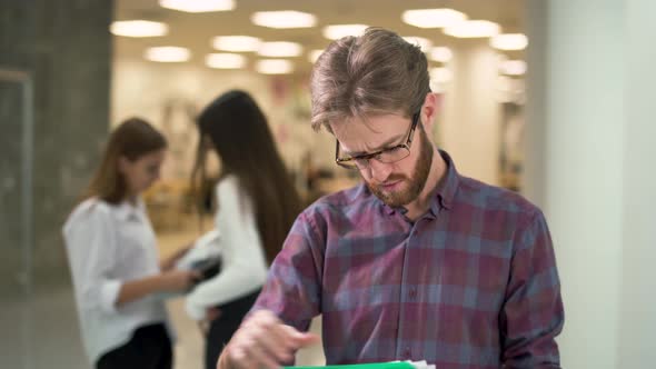 Portrait a Guy with a Beard in Glasses and Casual Plaid Shirt Reading Documents with Sales Reports alt