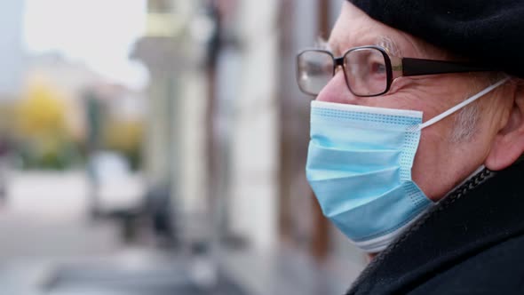 Portrait of a Sad Old Man with a Blue Mask and Beret Sitting in a City Park alt