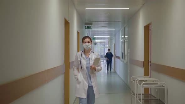 A Masked Doctor Walks Down the Corridor of the Hospital alt