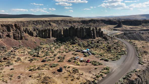 Orbiting drone shot of unique rock climbing feature with campers parked beneath. alt