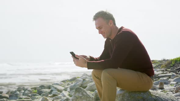 Caucasian man enjoying free time by sea on sunny day sitting on smartphone alt