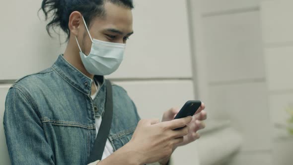 Young Asian man wearing a surgical mask and using smartphone.