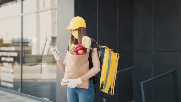 Young Delivery Worker Woman in Uniform Hat Medical Mask Gloves Holding Bag with alt