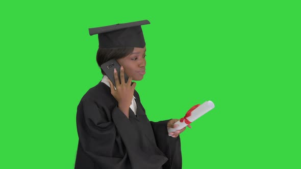African American Female Student in Graduation Robe Talking on the Phone While Walking on a Green alt