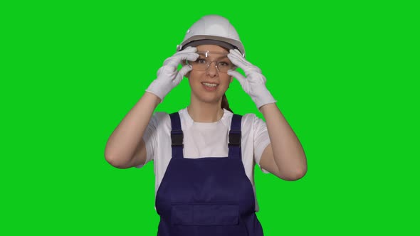Woman Builder in Blue Overalls and White Hard Hat Put on Protective Glasses