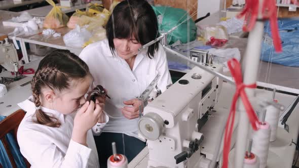 Grandma with Little Granddaughter Sew Clothes in the Factory alt