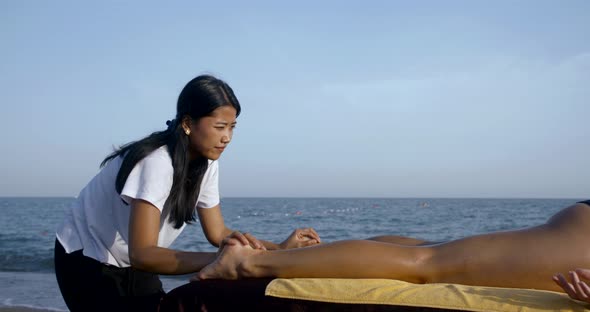 Close-up Massage on the Beach on a Special Table. Asian Masseuse Massages the Whole Legs, Buttocks alt