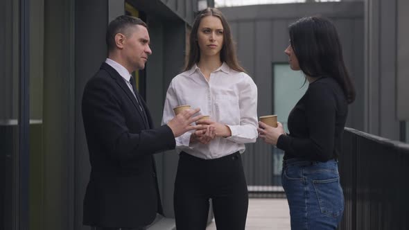 Slim Young Woman Standing with Coworkers Drinking Coffee on Break Outdoors Talking alt