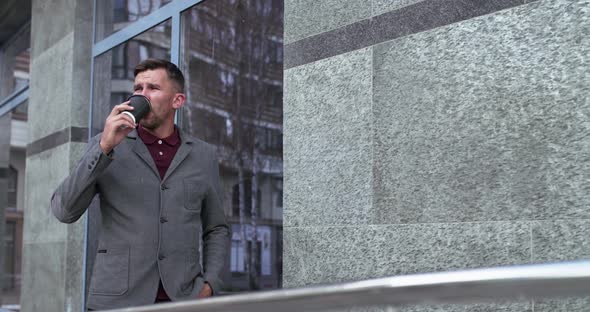 Thoughtful Man Drinks a Cup of Beverage and Looks Aside at Office Centre alt