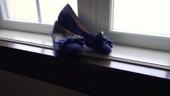 Slow push in shot of a bride's wedding shoes in a large window sill with the rings resting on top alt