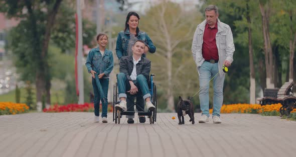 Guy in a Wheelchair Walks with His Family Along the Avenue
