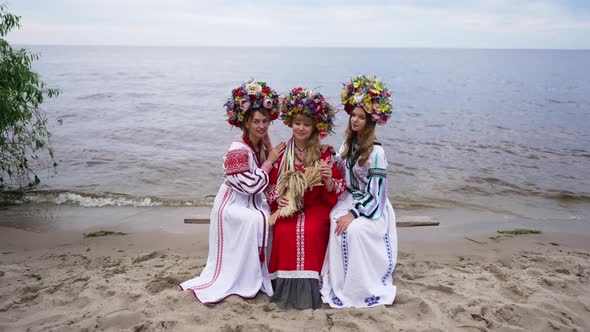 Wide Shot Portrait of Beautiful Ukrainian Women Sitting on River Shore Looking at Camera Smiling alt
