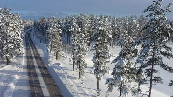 Closeup Aerial Shot of a Snowy Road Surrounded By Trees alt