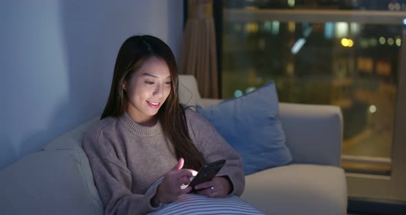 Woman look at mobile phone and sit on sofa at night