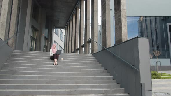 Young Muslim Woman Sitting on Stairs Near Business Center and Working on alt