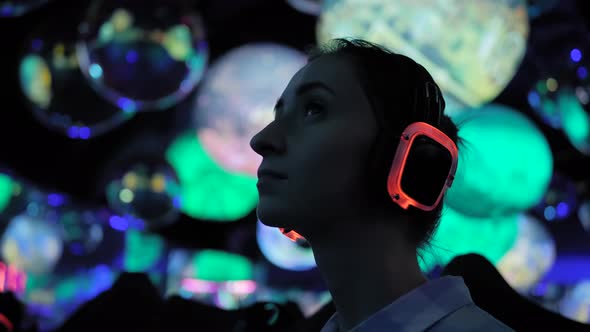 Woman Wearing Wireless Headphones at Exhibition or Museum with Colorful Light