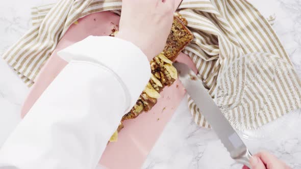 Flat lay. Slicing banana nut bread topped with caramel and garnished with banana chips and walnuts. alt