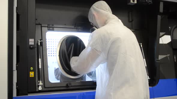 A Man in a White Protective Suit Stands Near a Large 3D Printer alt