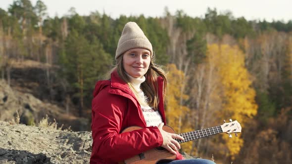 Woman Sits on Rock on and Holds the Ukulele