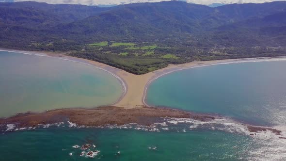 Aerial shot pulling away from the whale tail shaped rocky point of Punta Uvita surrounded by bright alt