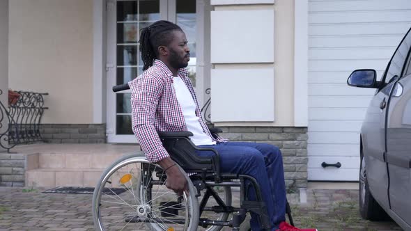 Side View African American Man Rolling Wheelchair to Car Opening Driver's Seat Door alt