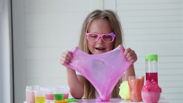Little girl stretching pink slime to the sides. Kids hands playing slime toy