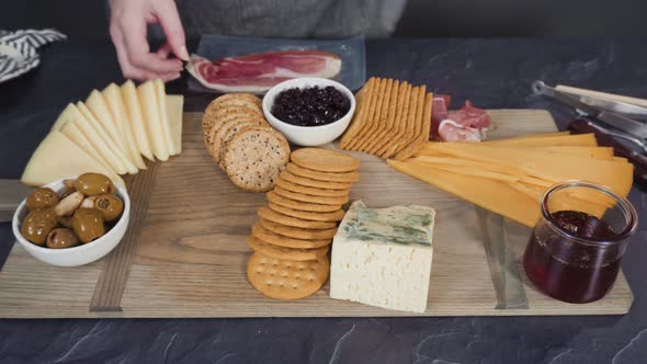Arranging gourmet cheese, crakers, and fruits on a board for a large cheese board. alt