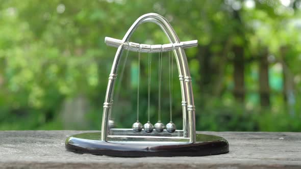 Newton's Cradle metal balls on green nature background, swinging metal balls, Close up. alt