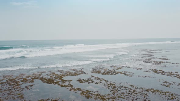 Aerial Flyby of Large Ocean Waves Following Each Other and Breaking Into White Foam on Stone Reef alt