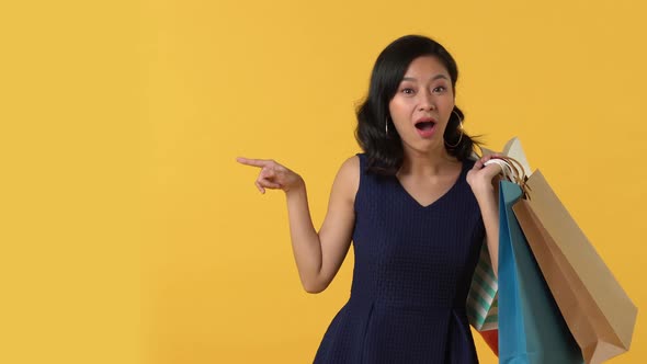 Surprised young asian woman with shopping bags pointing to copy space aside