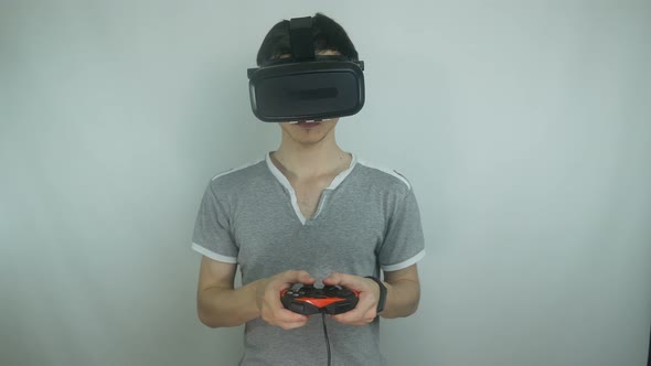 Guy Plays In The Helmet Of Virtual Reality In The Game Using The Gamepad