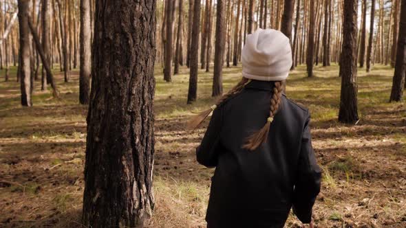 The Little Girl Runs Along the Path Road in the Pine Forest. Dressed in the Leather Jacket.